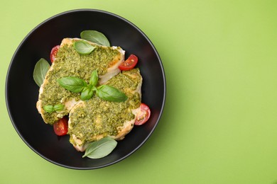 Photo of Delicious chicken breasts with pesto sauce, tomatoes and basil on light green table, top view. Space for text