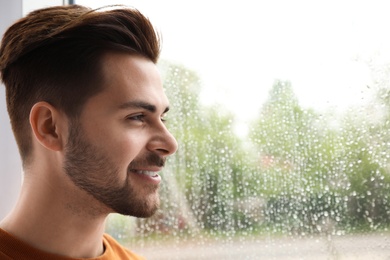 Photo of Smiling handsome man near window indoors on rainy day
