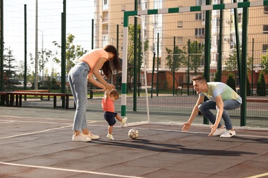 Photo of Happy family with adorable little baby playing football outdoors