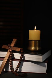 Photo of Church candle, Bible, rosary beads and cross on table in darkness