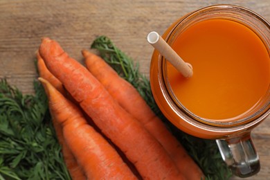 Photo of Freshly made carrot juice in mason jar with straw on wooden table, top view