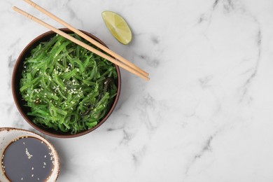 Photo of Tasty seaweed salad in bowl served on white marble table, flat lay. Space for text