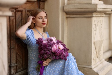 Beautiful woman with bouquet of spring flowers near building outdoors, space for text