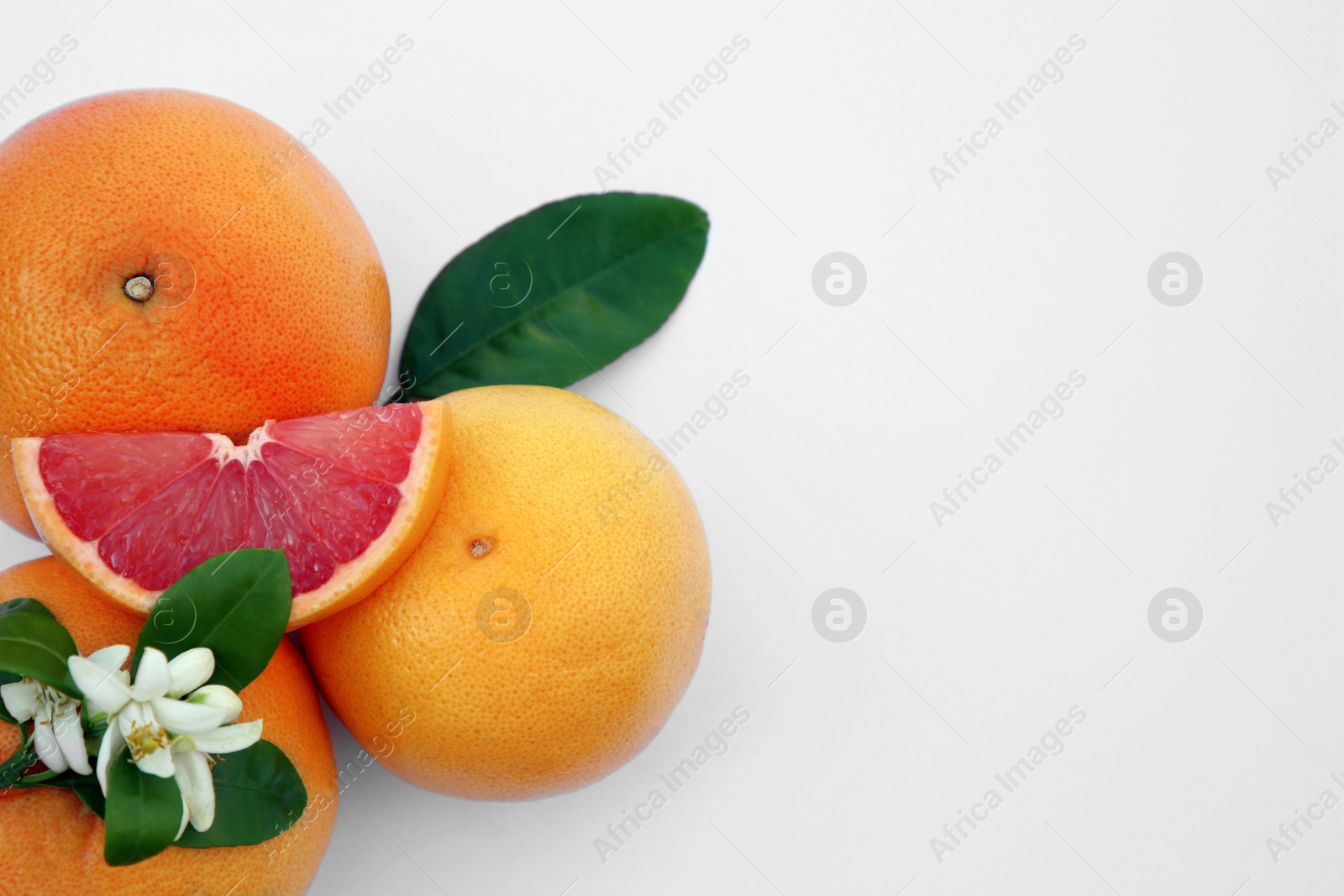 Photo of Fresh ripe grapefruits and green leaves on white background, top view. Space for text