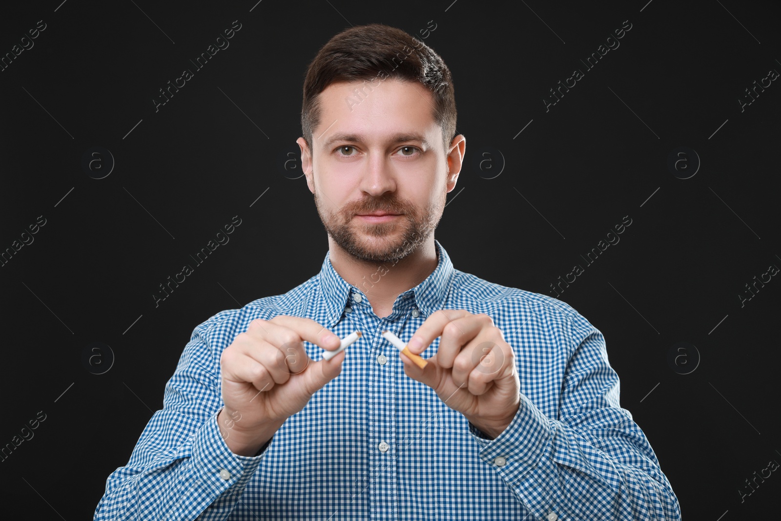 Photo of Stop smoking concept. Man holding pieces of broken cigarette on black background