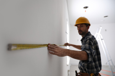 Worker measuring white wall indoors, focus on hand