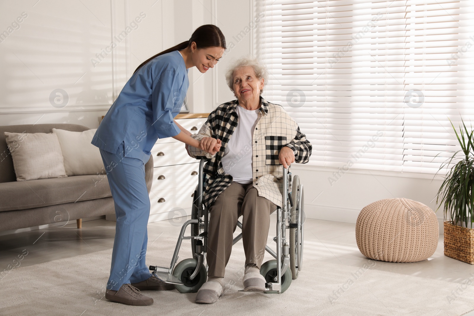 Photo of Young caregiver assisting senior woman in wheelchair indoors. Home health care service