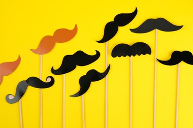 Photo of Fake paper mustaches with sticks on yellow background, flat lay