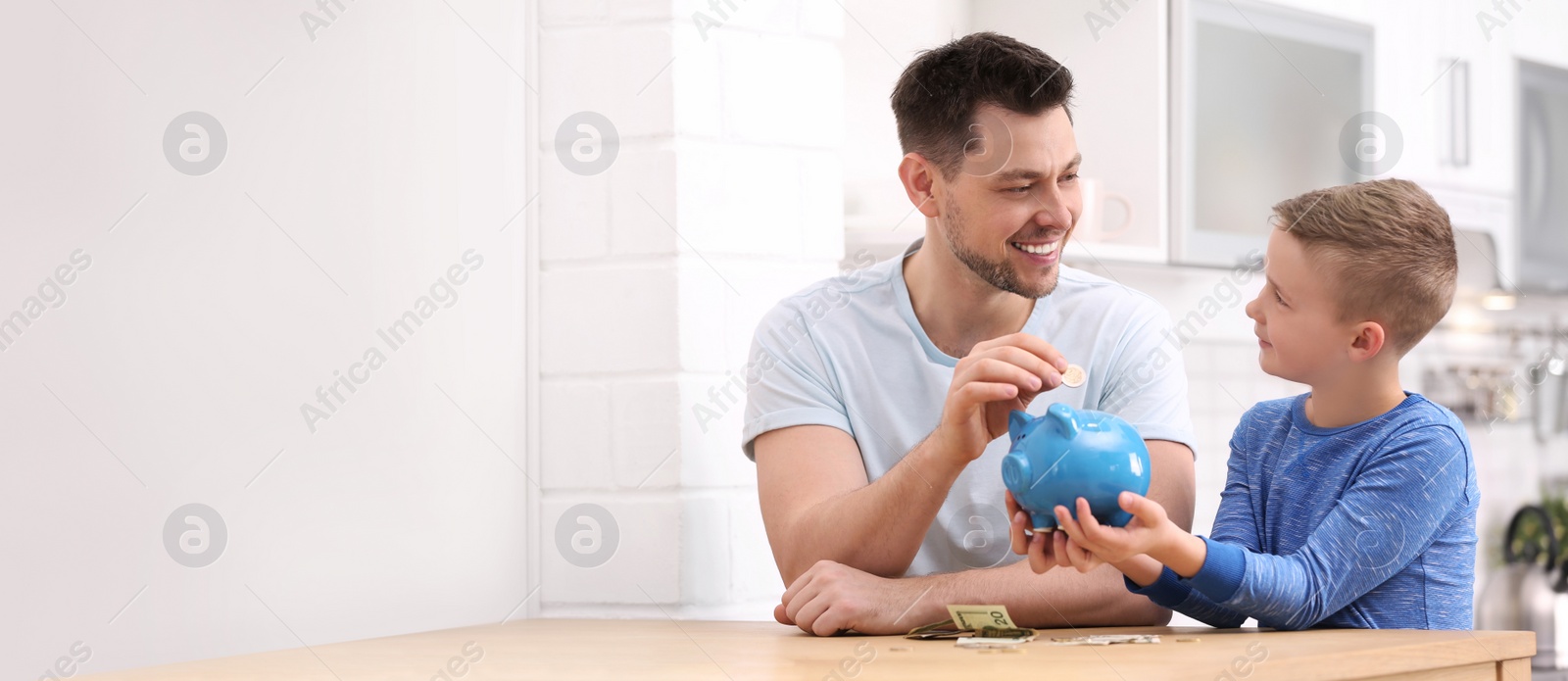 Image of Father and son putting money in piggy bank at home, space for text. Banner design