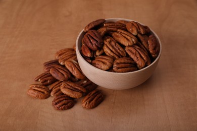 Photo of Bowl and tasty pecan nuts on wooden table