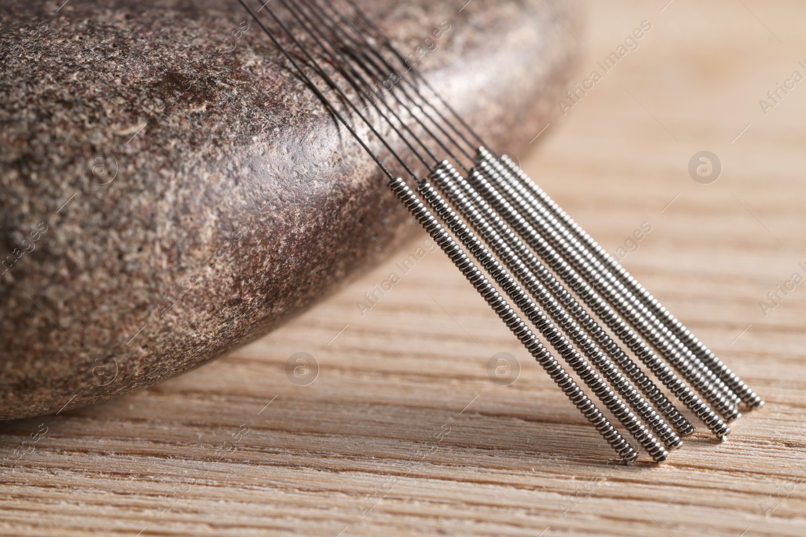 Photo of Acupuncture needles and spa stone on wooden table, closeup