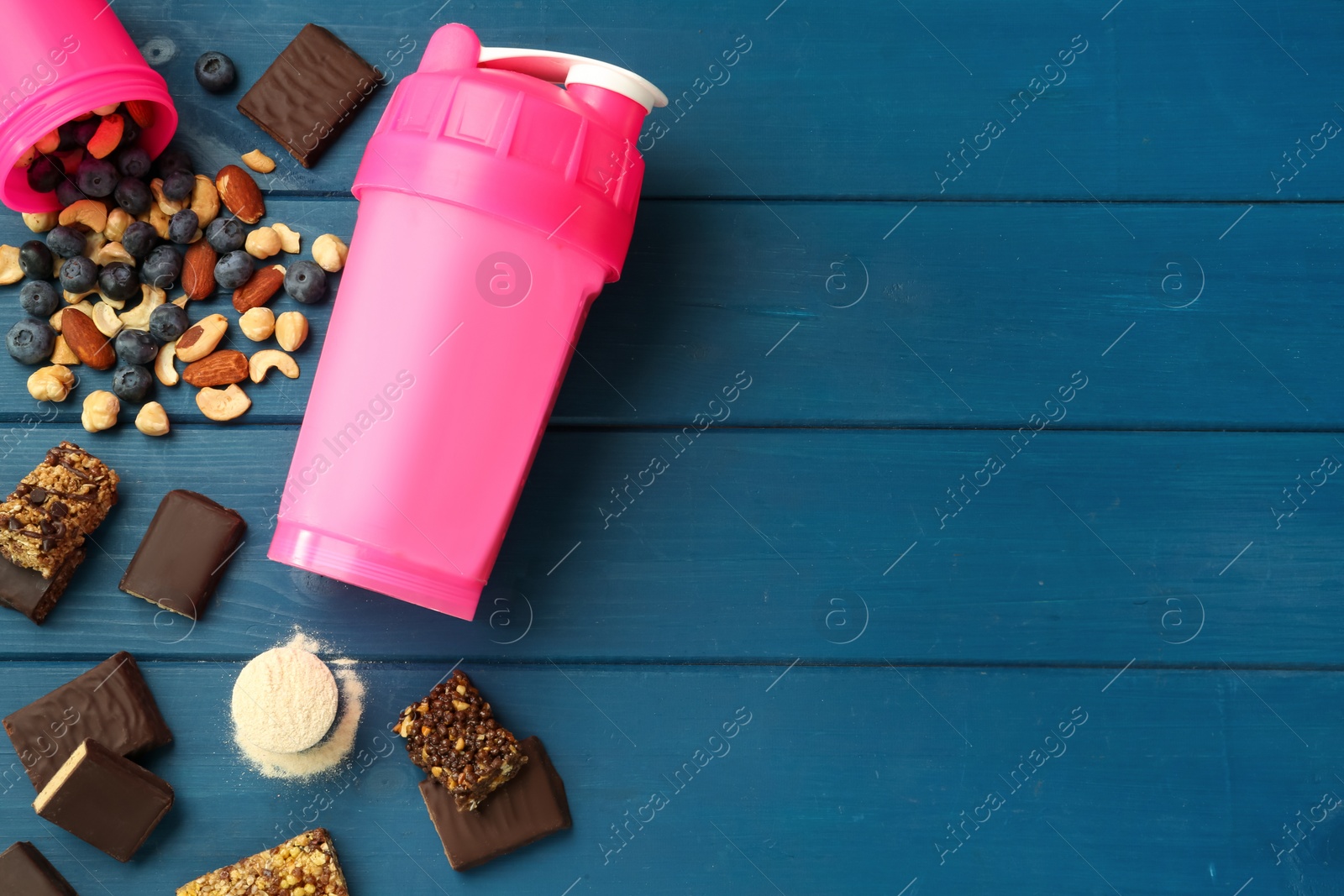 Photo of Different energy bars, nuts, blueberries, protein cocktail and powder on blue wooden table, flat lay. Space for text
