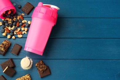 Different energy bars, nuts, blueberries, protein cocktail and powder on blue wooden table, flat lay. Space for text