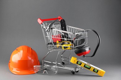 Photo of Small shopping cart with set of construction tools. protective glasses and hard hat on grey background