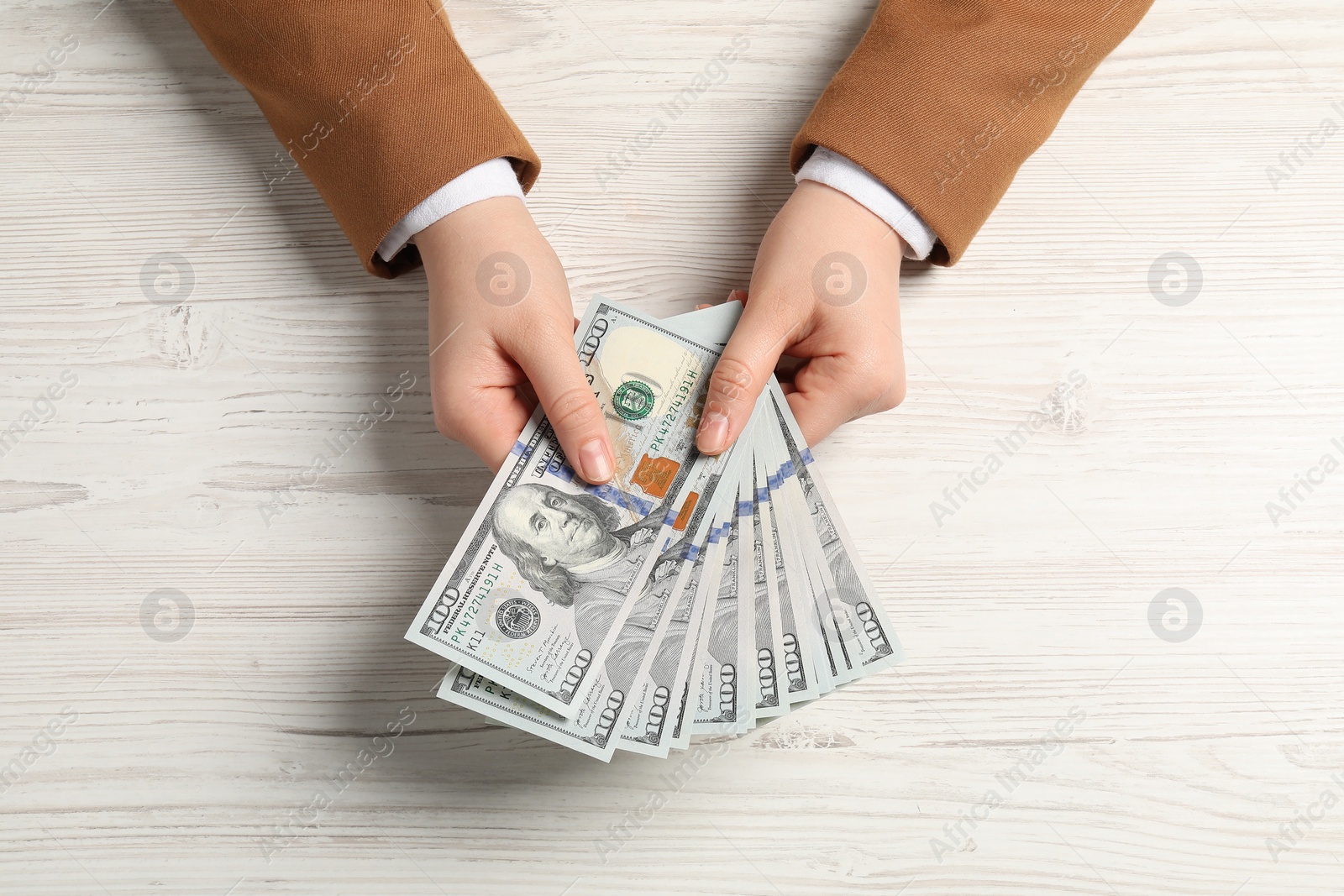 Photo of Money exchange. Woman holding dollar banknotes at white wooden table, top view