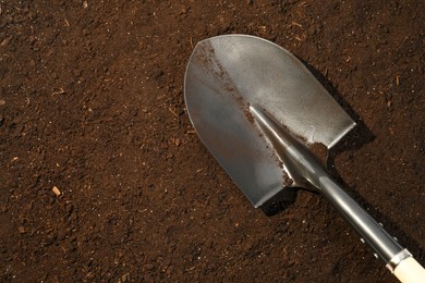 Photo of Metal shovel on fertile soil, top view and space for text. Gardening tool
