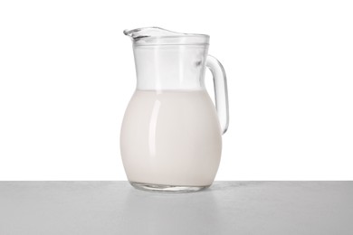 Jug of tasty milk on light table against white background