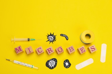 Photo of Word Microbes made with wooden cubes, pictures, syringe and thermometer on yellow background, flat lay. Space for text