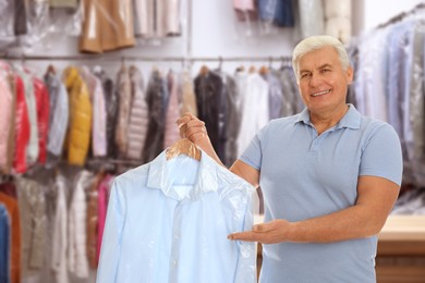 Image of Dry-cleaning service. Happy man holding hanger with shirt in plastic bag indoors
