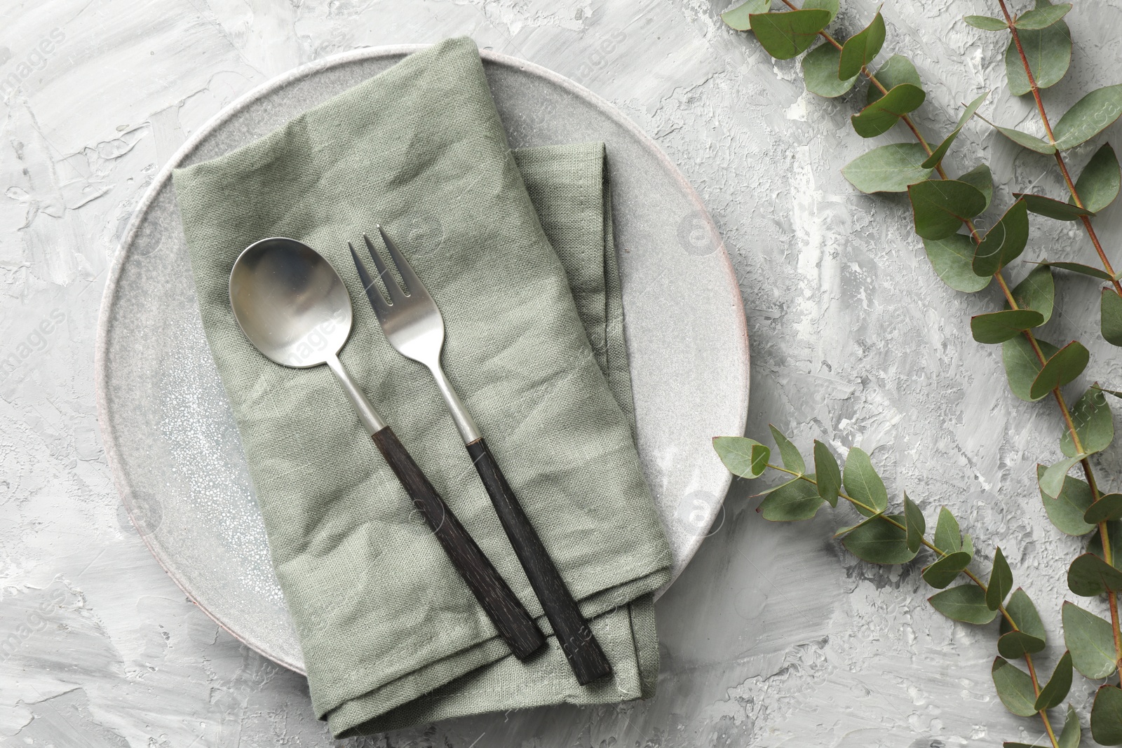 Photo of Stylish setting with cutlery, napkin, eucalyptus branches and plate on grey textured table, flat lay