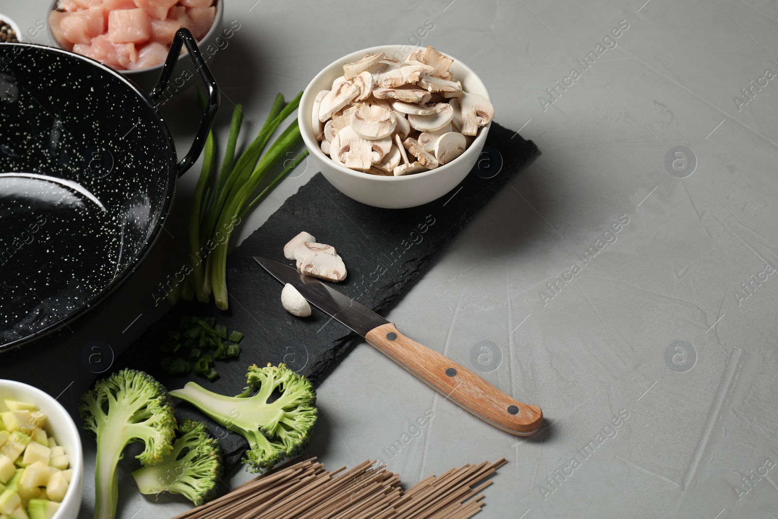 Photo of Wok pan, noodles, chicken and other products on light grey table. Space for text