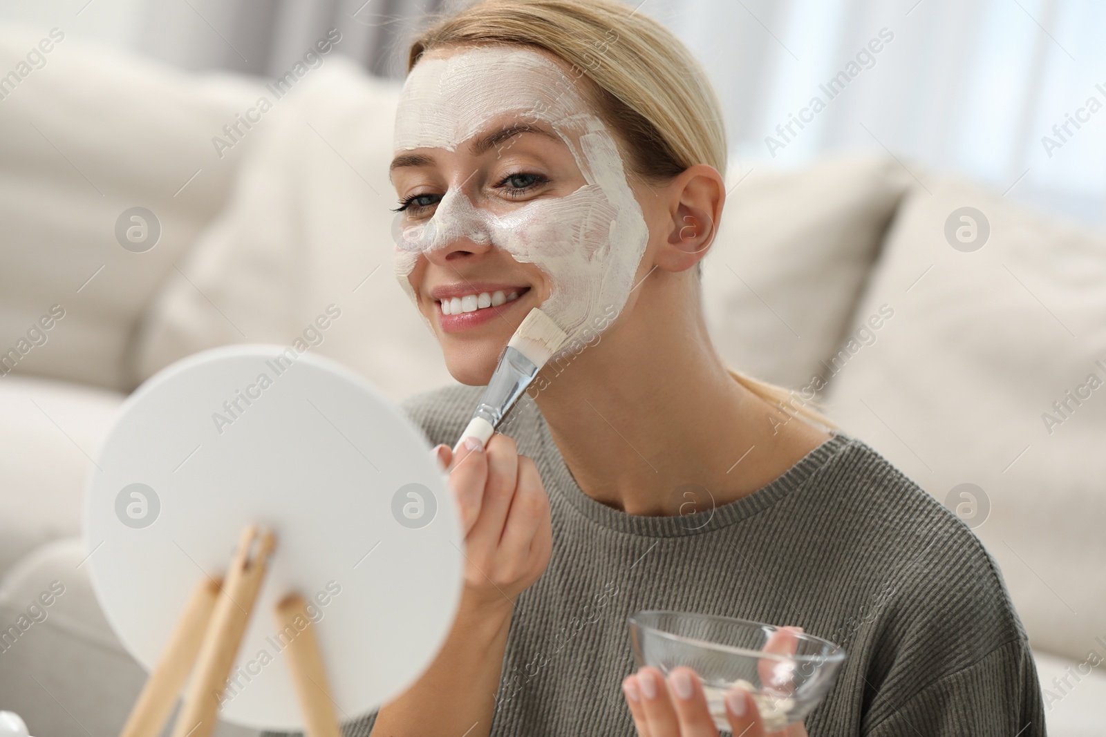 Photo of Young woman applying face mask in front of mirror at home. Spa treatments