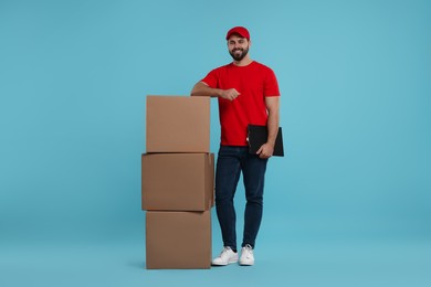 Happy courier with clipboard and stack of parcels on light blue background