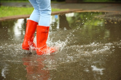 Photo of Woman with red rubber boots jumping in puddle, closeup. Rainy weather