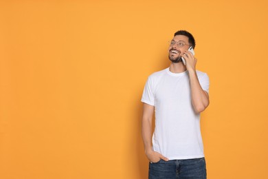 Photo of Handsome man talking on smartphone against orange background. Space for text
