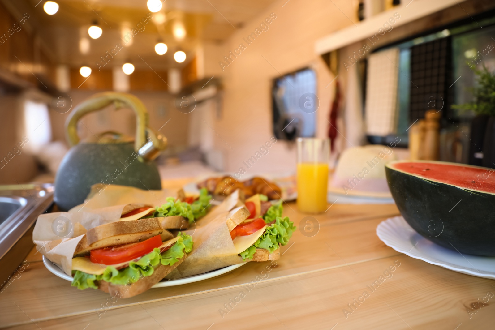 Photo of Delicious sandwiches and watermelon on wooden table in modern trailer. Camping vacation