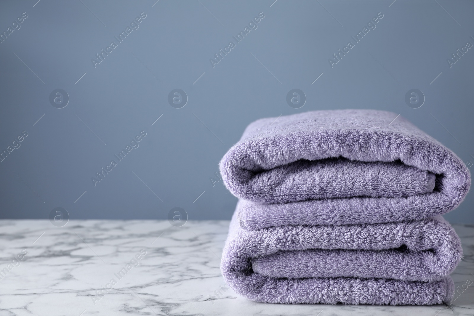 Photo of Stack of clean bath towels on white marble table. Space for text