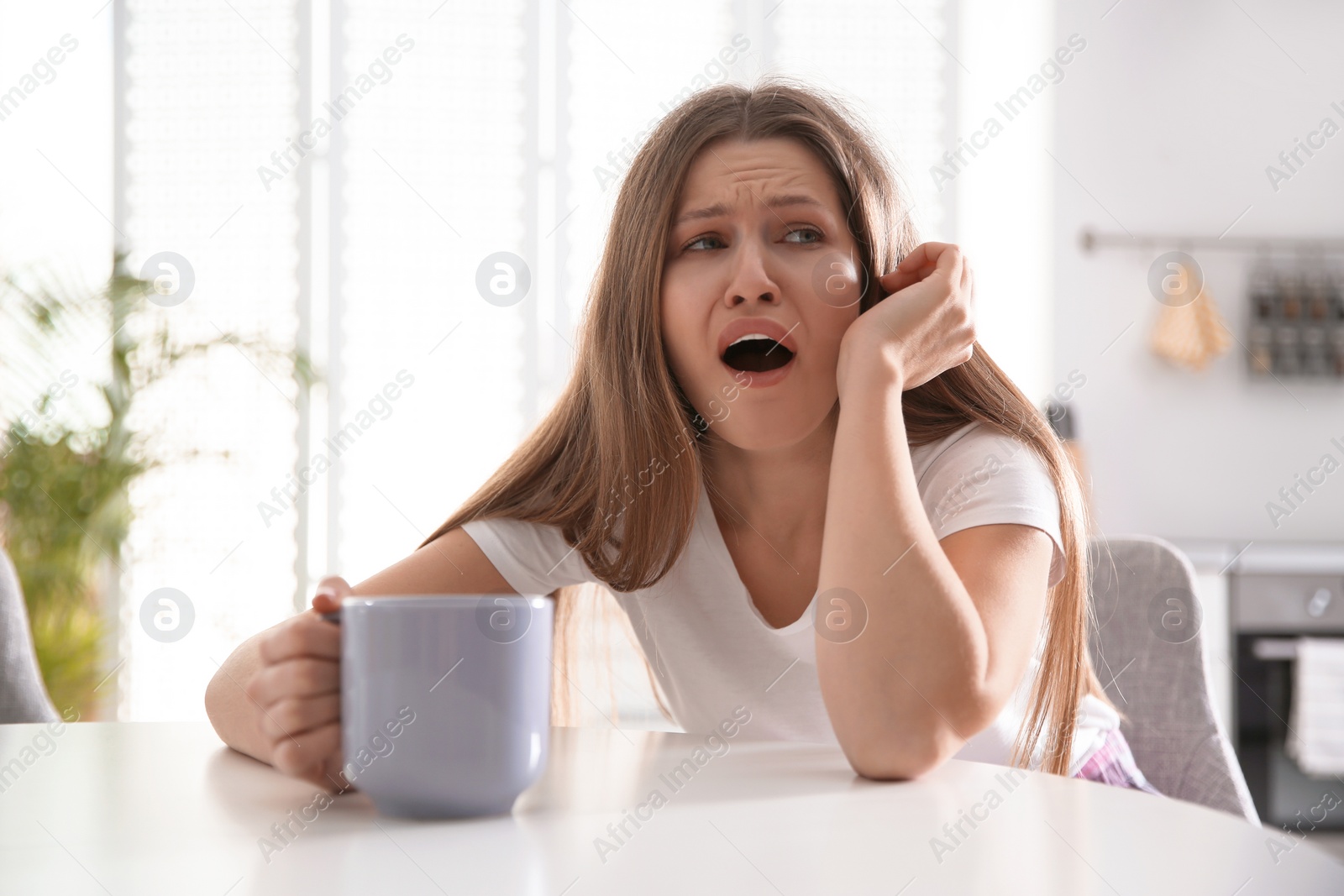 Photo of Sleepy young woman with cup of drink at home in morning