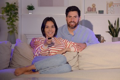Happy couple watching TV on sofa at home