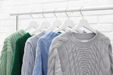 Collection of warm sweaters hanging on rack near brick wall