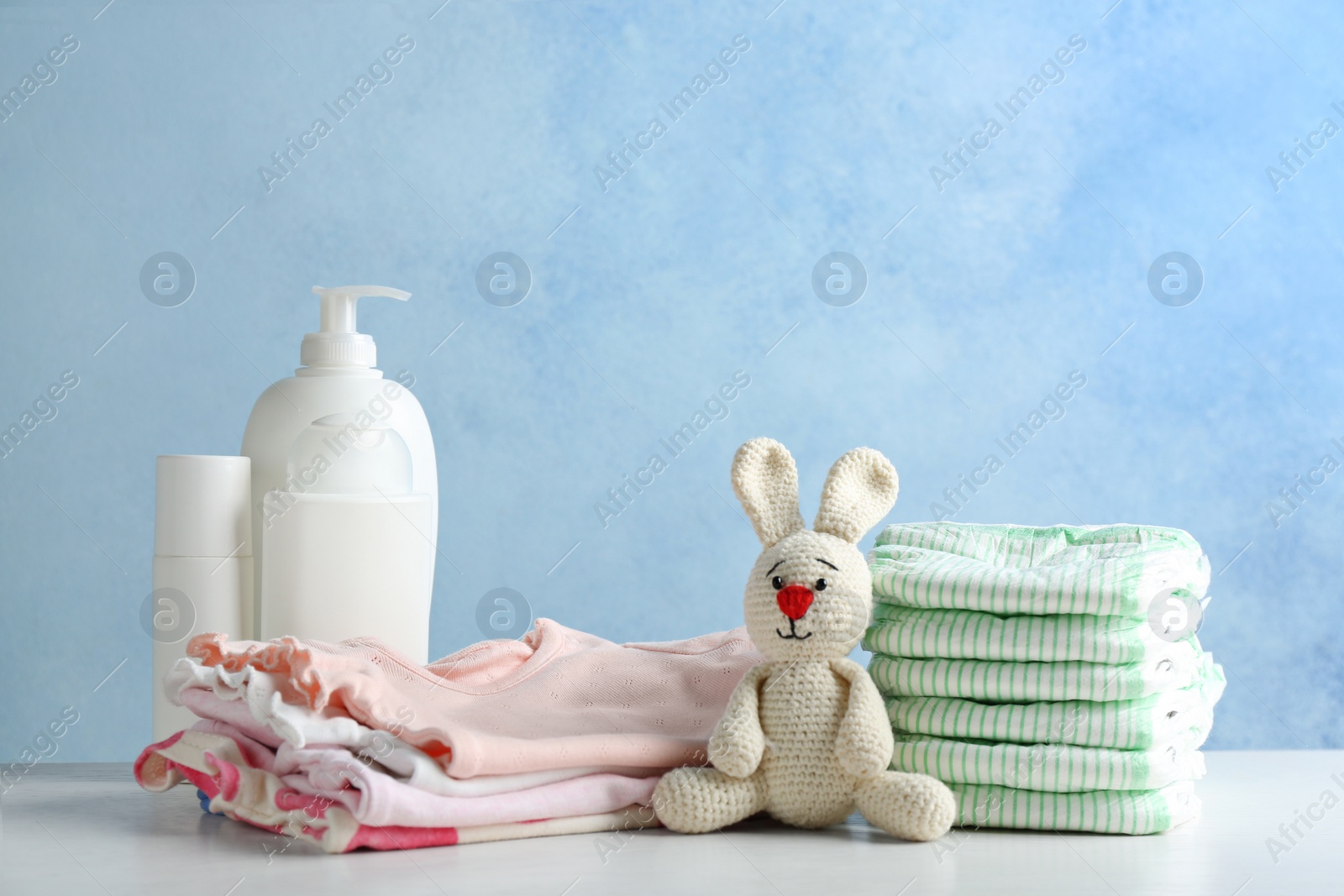 Photo of Stack of diapers and baby accessories on table against color background. Space for text