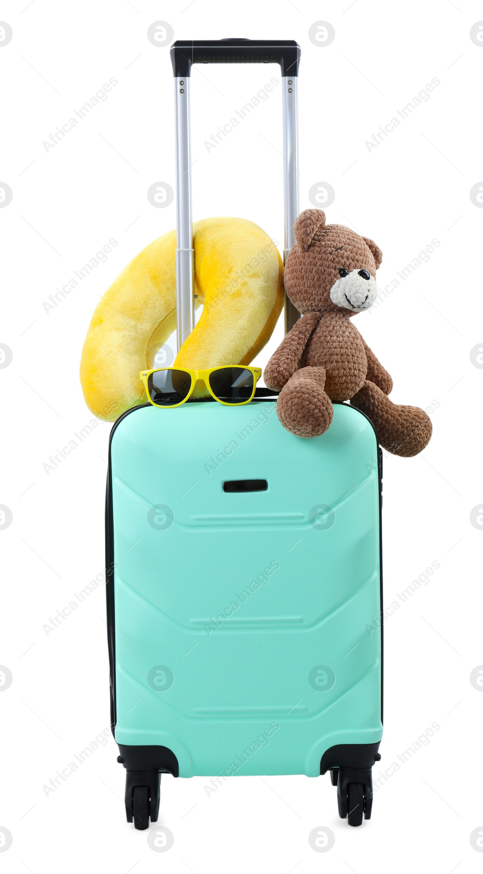 Photo of Soft travel pillow and toy bear on turquoise suitcase isolated on white