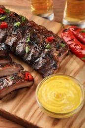 Tasty grilled ribs and sauce on wooden table, closeup