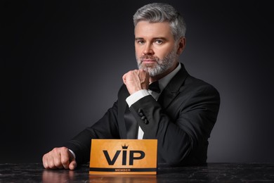 Photo of Handsome man sitting at table with VIP sign on black background