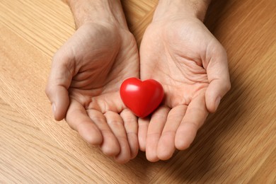 Man holding red heart in hands at wooden table, closeup