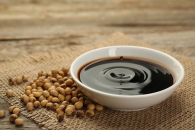 Photo of Soy sauce in bowl and beans on wooden table, closeup. Space for text