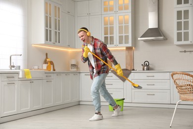Photo of Handsome young man with headphones singing while cleaning kitchen