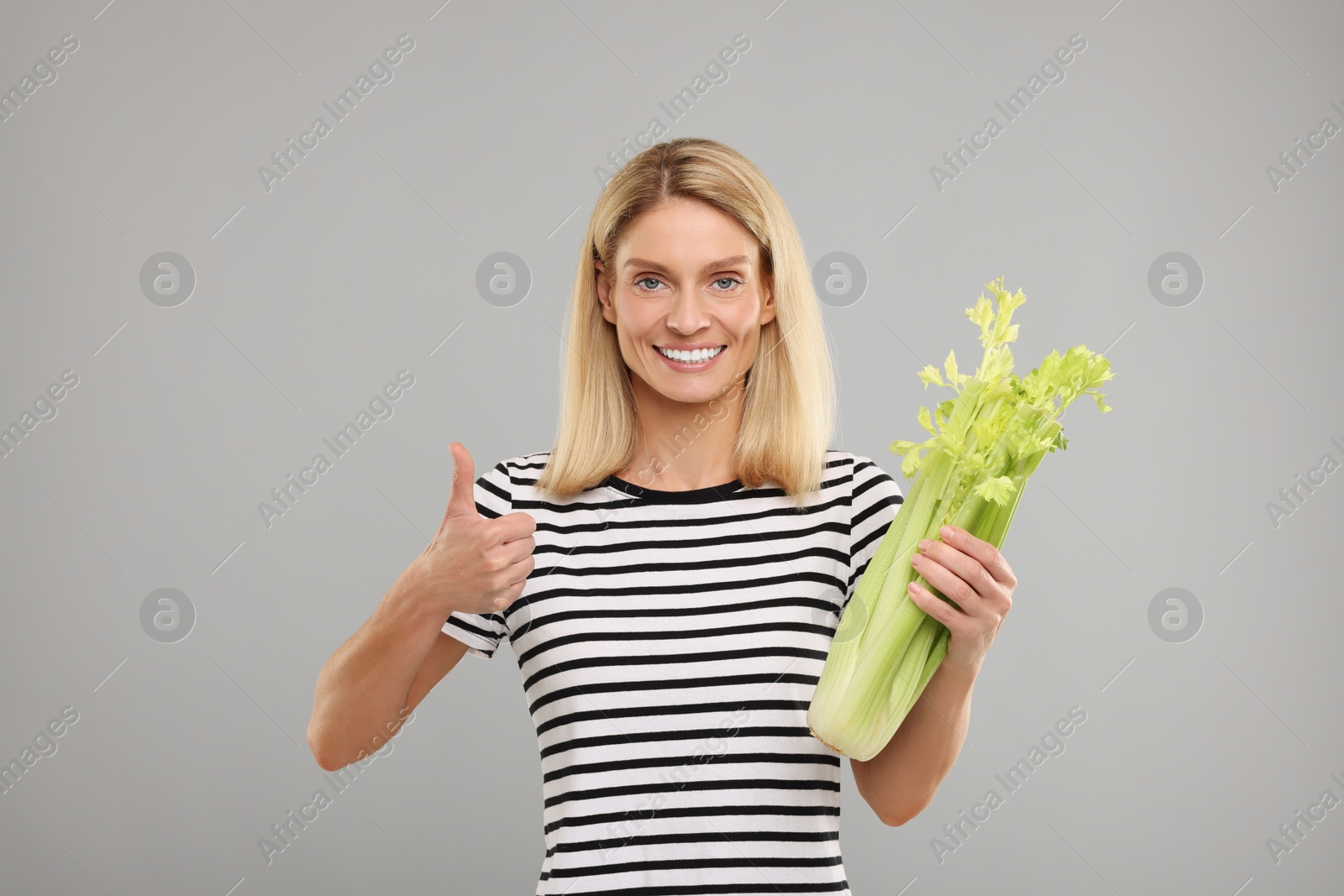 Photo of Woman with fresh green celery bunch showing thumb up against light grey background