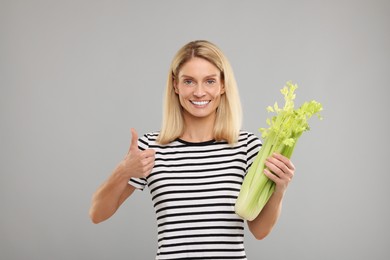 Photo of Woman with fresh green celery bunch showing thumb up against light grey background