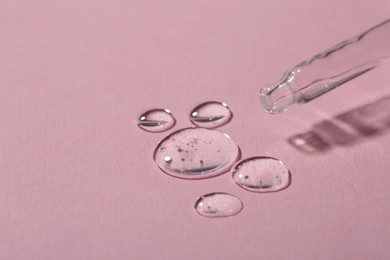 Photo of Dripping cosmetic serum from pipette onto pink background, macro view. Space for text
