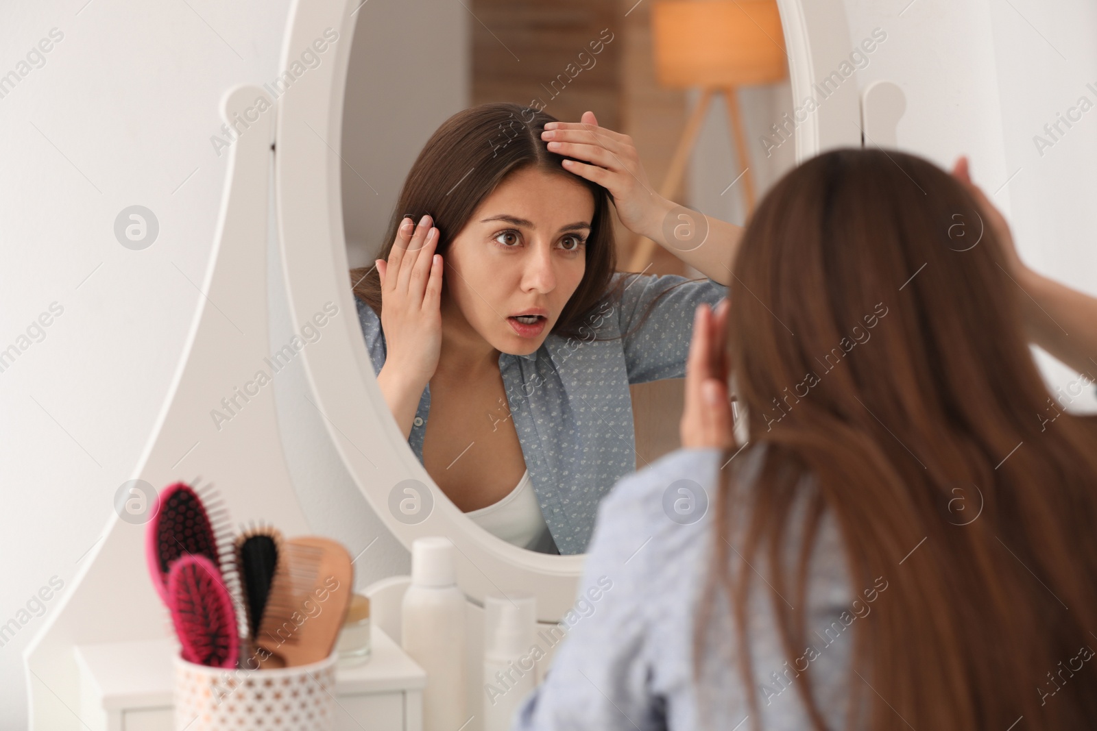 Photo of Emotional woman with hair loss problem looking in mirror indoors