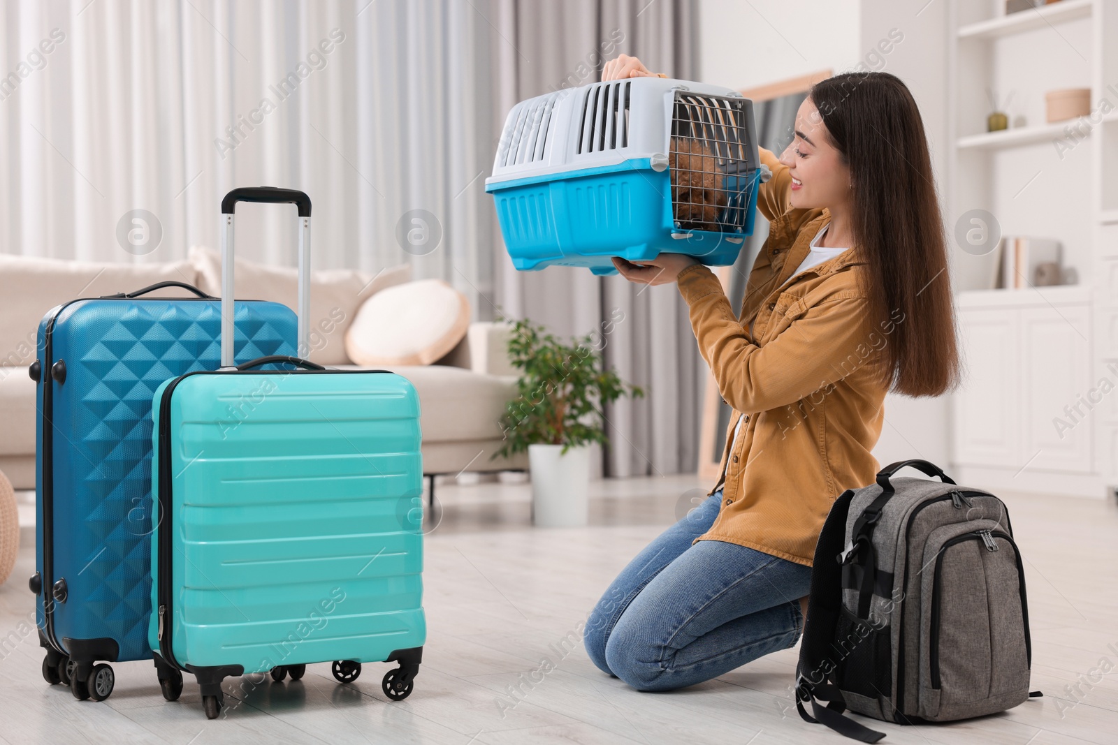 Photo of Travelling with pet. Smiling woman looking at carrier with her dog indoors