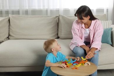 Motor skills development. Happy mother helping her son to play with colorful wooden arcs at coffee table in room. Space for text