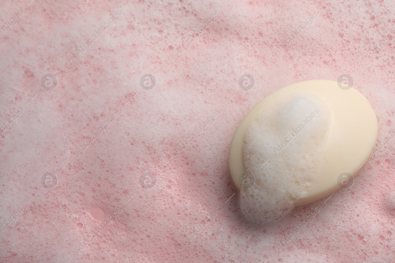 Photo of Soap with fluffy foam on pink background, top view. Space for text