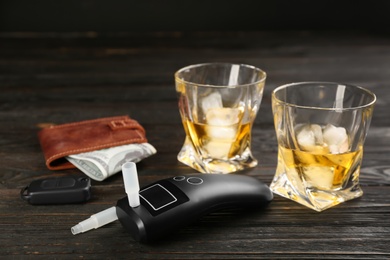 Photo of Modern breathalyzer, car key, alcohol and wallet on dark wooden background