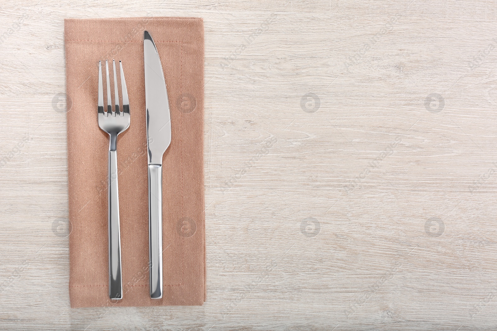 Photo of Shiny fork, knife and napkin on white wooden table, flat lay. Space for text